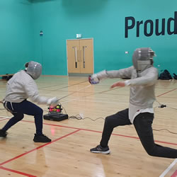 Two fencers mid-fight during a fencing match using Sabre weapons.